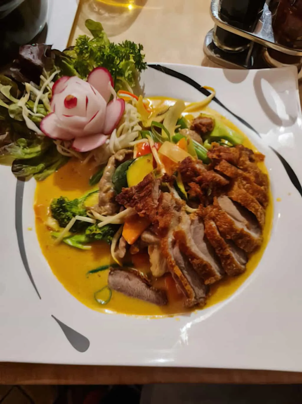 Knusprige Ente mit gelber Currysoße, angerichtet mit Salat